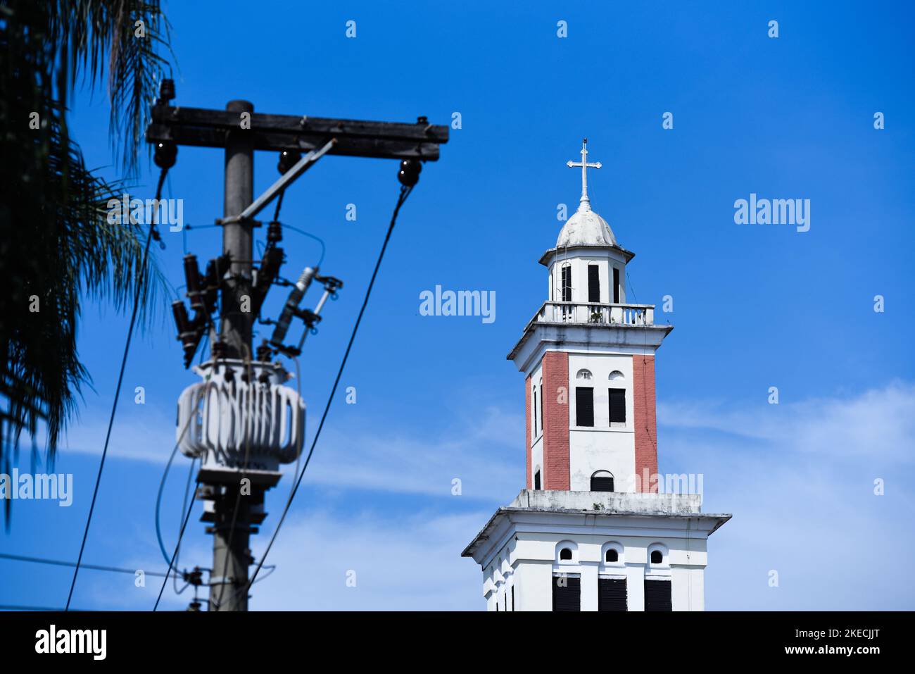 Trasformatore elettrico con cavi e Campanile di una Chiesa nel cielo blu Foto Stock