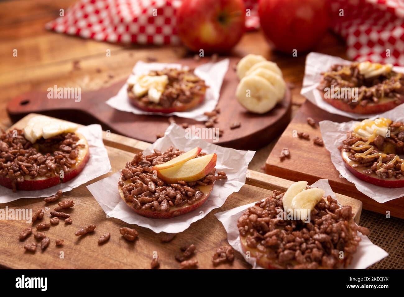 Festa creativa snack per le vacanze. Le mele si arrotolano con burro di arachidi, caramello e cioccolato farcitura di riso soffiato con fette di banana. Appetiz divertente Foto Stock