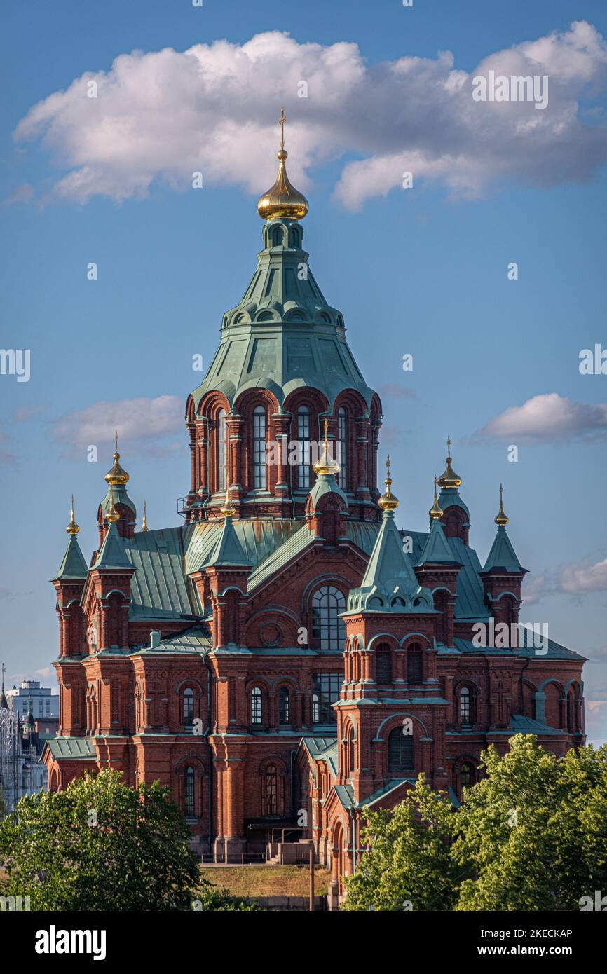 Helsinki, Finlandia - 20 luglio 2022: Cattedrale di Uspenski. Primo piano dell'edificio in mattoni rossi e cupola verde sopra il verde del fogliame sotto il paesaggio azzurro Foto Stock