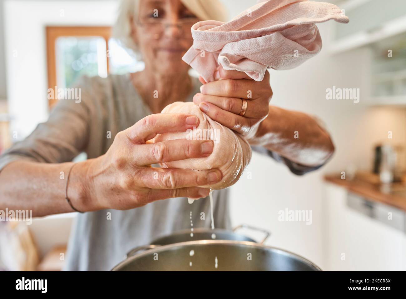 Fare paniere, donna spremitura un cheesecloth ripieno di formaggio cremoso e separare il formaggio dal siero di latte Foto Stock