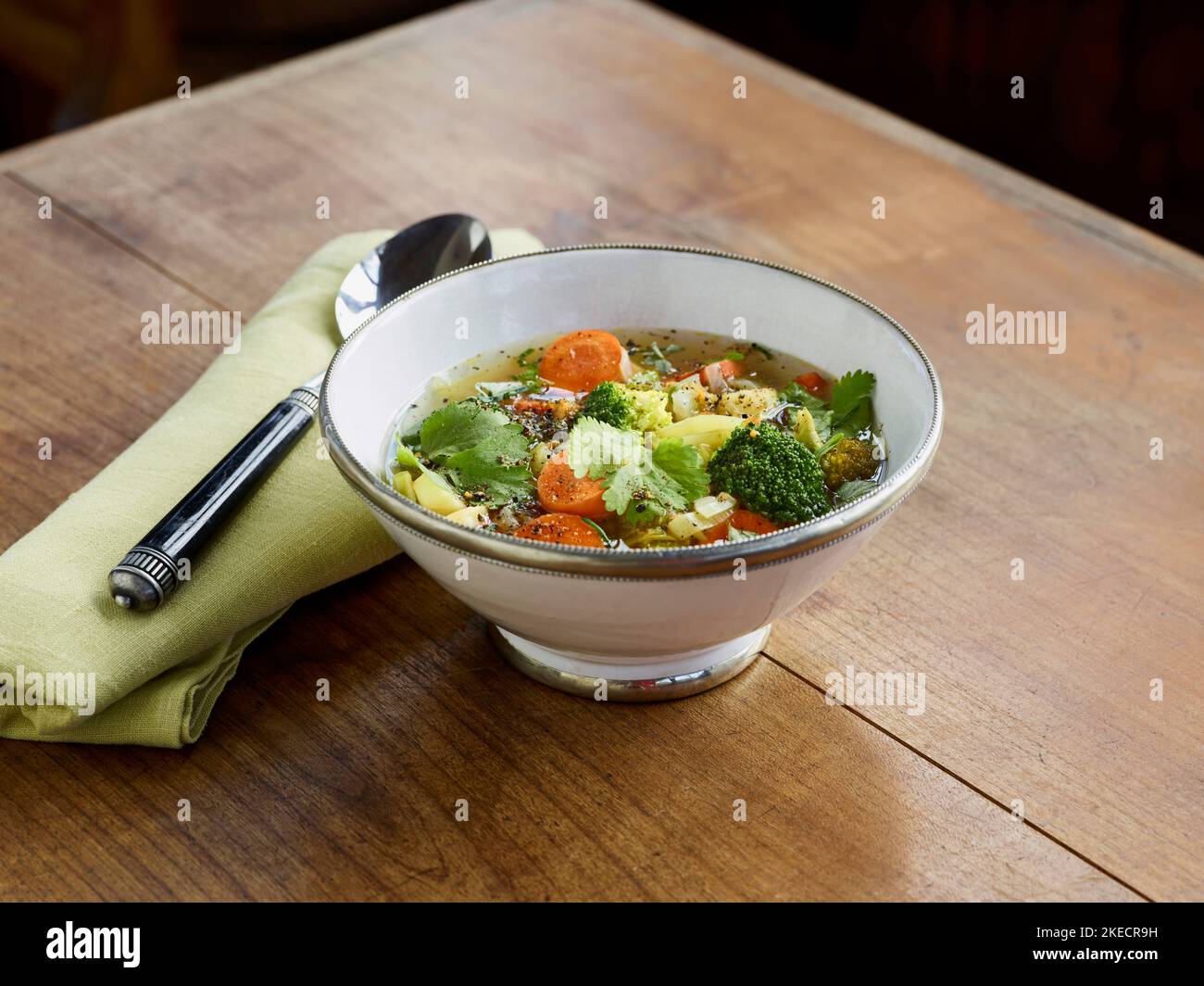 cucina ayurvedica, zuppa di verdure in ciotola bianca con bordo in argento su tavolo in legno Foto Stock