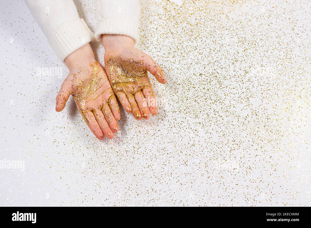 Le mani del bambino che tengono i glitter dorati su fondo bianco brillante. Luminoso Natale e Capodanno foto. piatto Lay. Vista dall'alto, disposizione piatta Foto Stock