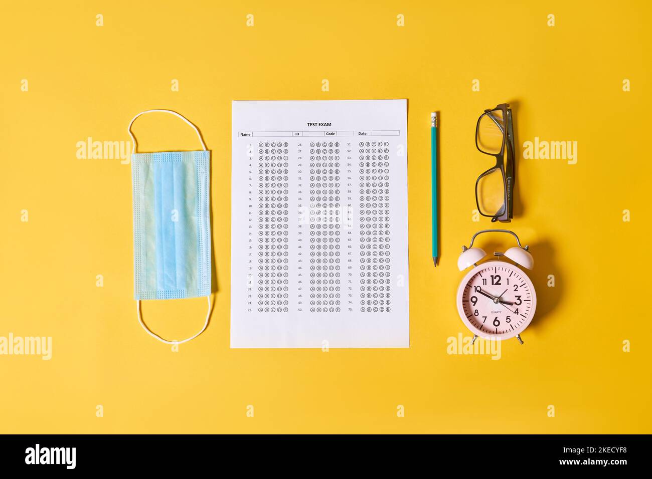 una scrivania da ufficio con un orologio, occhiali e un foglio di carta accanto ad esso su uno sfondo giallo Foto Stock