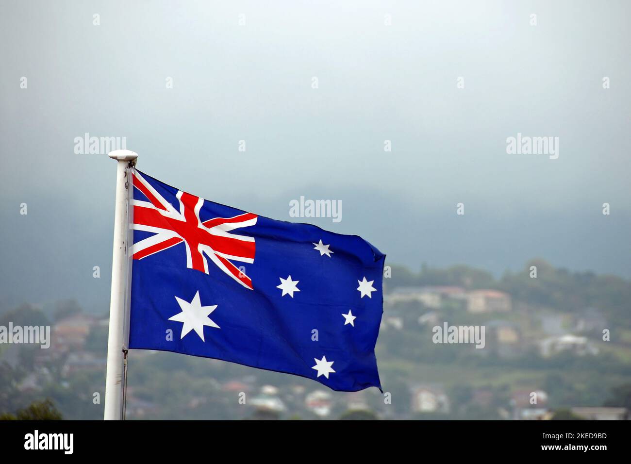 Bandiera australiana su uno sfondo di case su una collina e cielo. La bandiera australiana è composta da sei stelle e dal jack sindacale britannico. Foto Stock