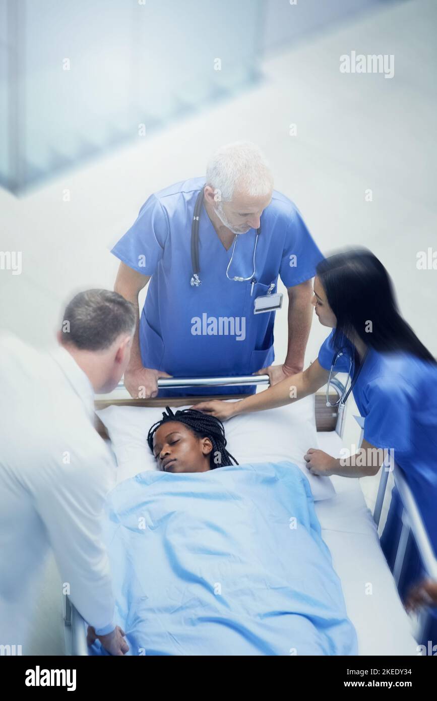 Ha bisogno di cure mediche immediate, un gruppo di medici che guardano un paziente su una gurney in un corridoio ospedaliero. Foto Stock