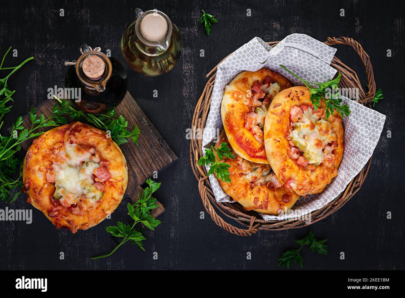 Mini pizza per bambini, piccole torte aperte con prosciutto, salsa di pomodoro, mozzarella e formaggio in cestino su fondo scuro. Vista dall'alto Foto Stock