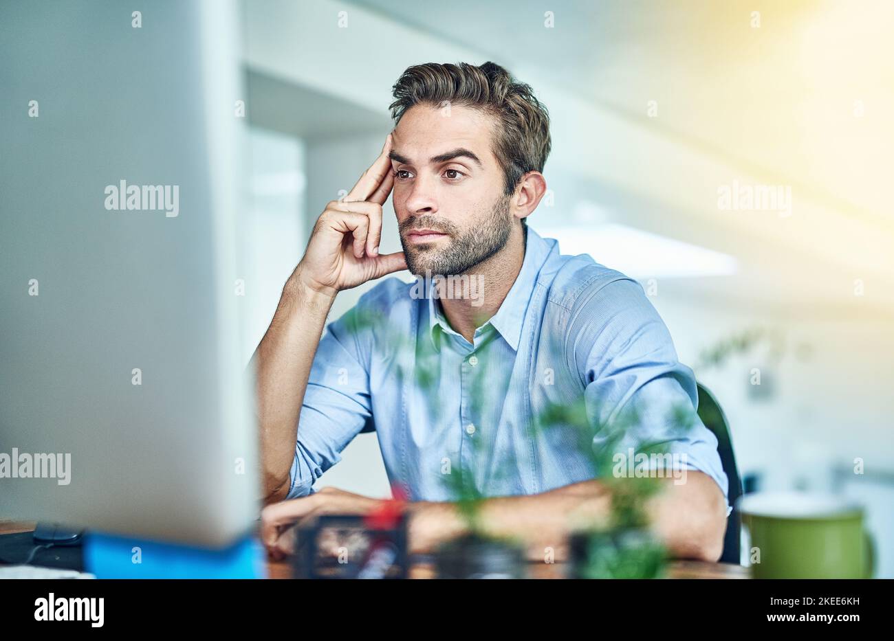 Perso in pensieri di successo. Un giovane uomo d'affari che lavora su un computer in un ufficio. Foto Stock