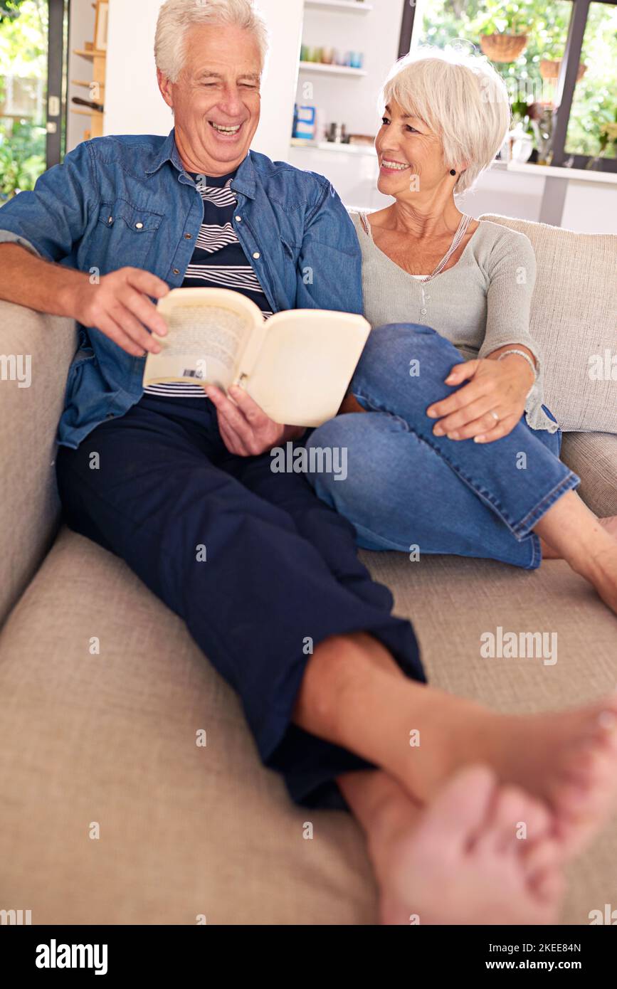 Le vere storie d'amore si avverano. Una coppia anziana rilassata che legge un libro insieme sul divano di casa. Foto Stock