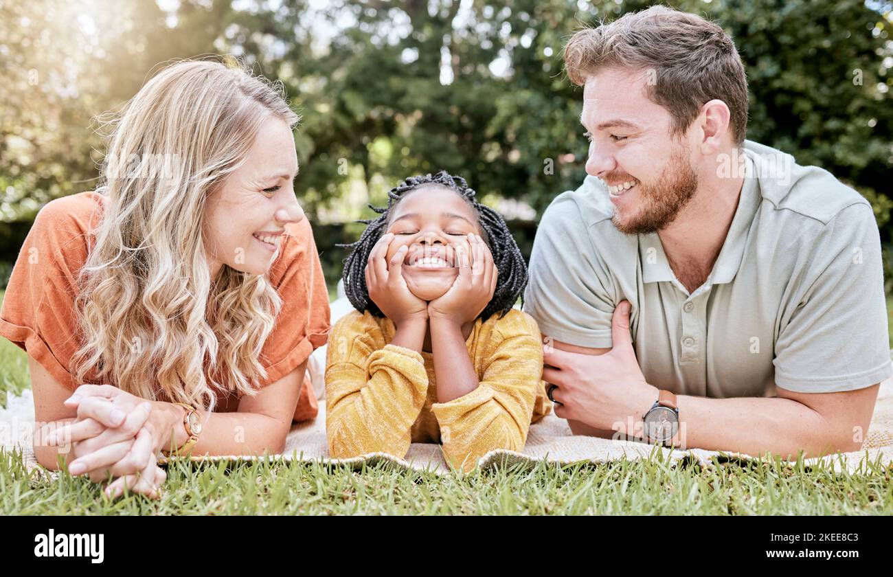 Famiglia, diversità e bambini con genitori adottivi e figlia adottiva insieme in un parco durante l'estate. Bambini, amore e adozione con una madre Foto Stock