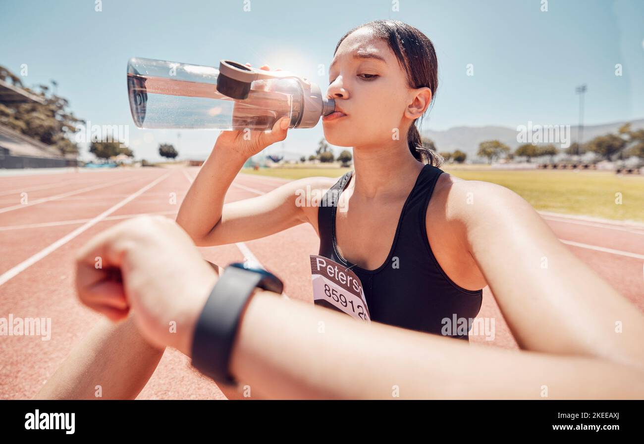 Bere acqua, tempo e correre con una donna sportiva che controlla il suo orologio durante un allenamento in pista. Fitness, esercizio fisico e idratazione con una donna Foto Stock