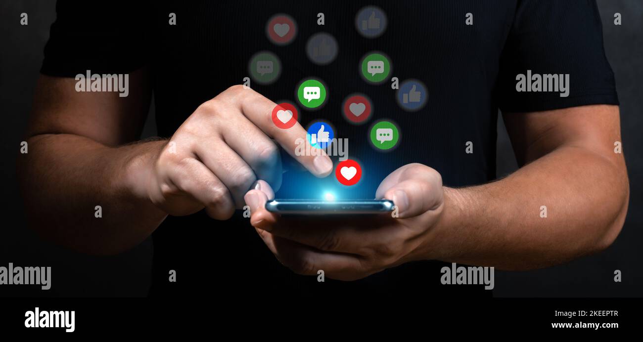 uomo mano tenere telefono con icona di social media virtuale. mani maschio tenere telefono cellulare con ologrammi di icone social network e applicazioni, cuori, li Foto Stock