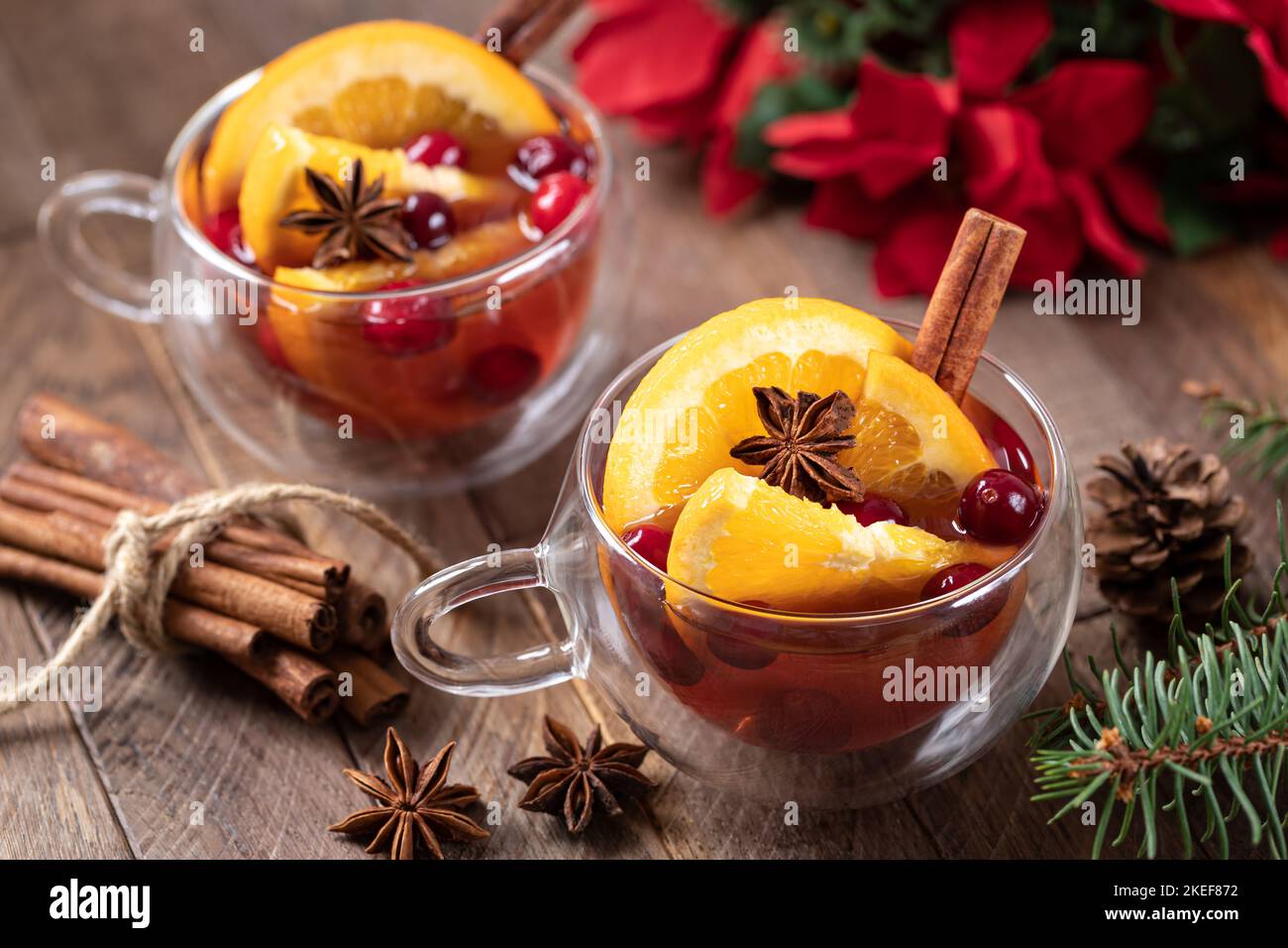 VIN brulé con fettine d'arancia, mirtilli rossi e spezie su un rustico tavolo di legno e decorazione di vacanza sullo sfondo Foto Stock