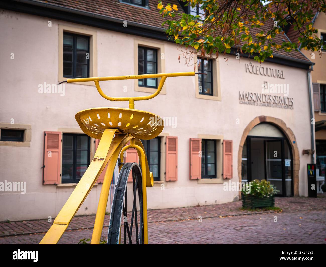 Rouffach, Francia - 11 ottobre 2022: Una grande bicicletta gialla storica di fronte a un centro culturale e centro di servizi a Rouffach, Alsazia Foto Stock