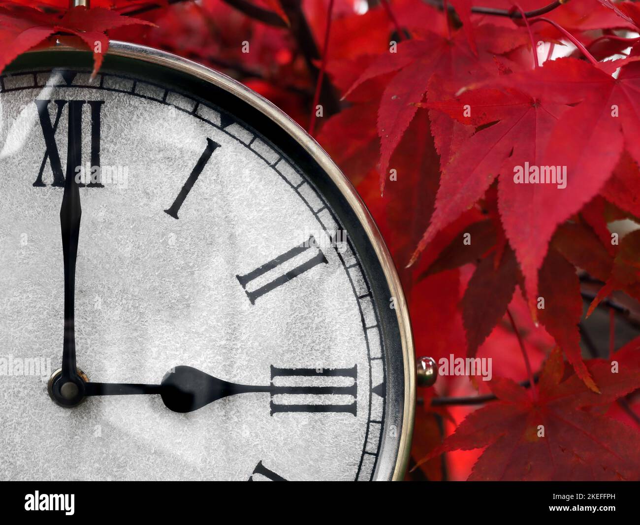 primo piano di un vecchio orologio della stazione ferroviaria con i numeri romani che mostrano le ore 3 di fronte alle foglie rosse autunno, concetto di cambiamento di tempo nel mese di ottobre Foto Stock