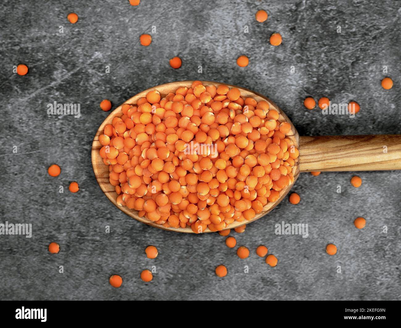 Lenticchie rosse in un cucchiaio da cucina in legno su sfondo grigio, sano concetto di cibo vegano con alte proteine Foto Stock
