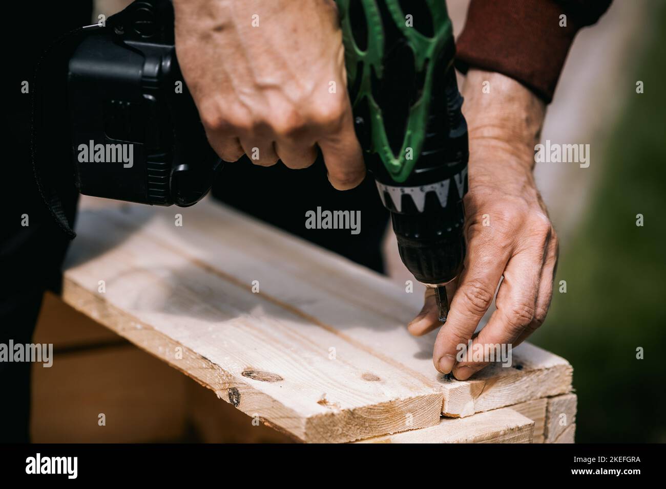 Man sta avvitando la vite nella scatola di legno con un cacciavite a batteria. Riparazione del prodotto con un cacciavite elettrico professionale. Primo piano. Foto di alta qualità Foto Stock