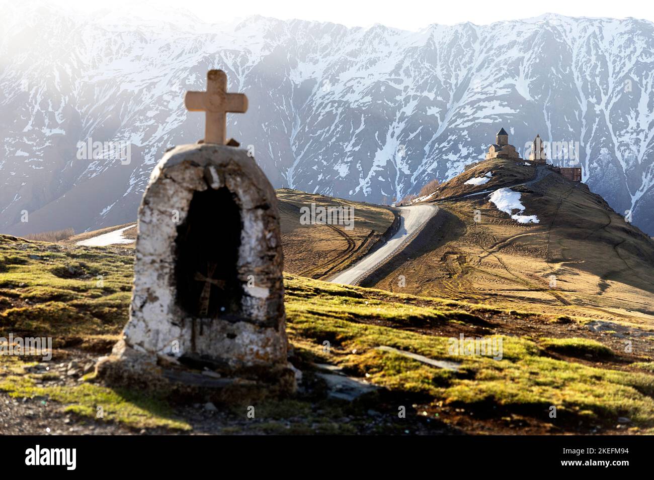 Piccola cappella e Gergeti Trinity Church sul retro in primavera luce mattutina con montagna innevata sul retro, Kazbegi, Georgia, Europa Foto Stock