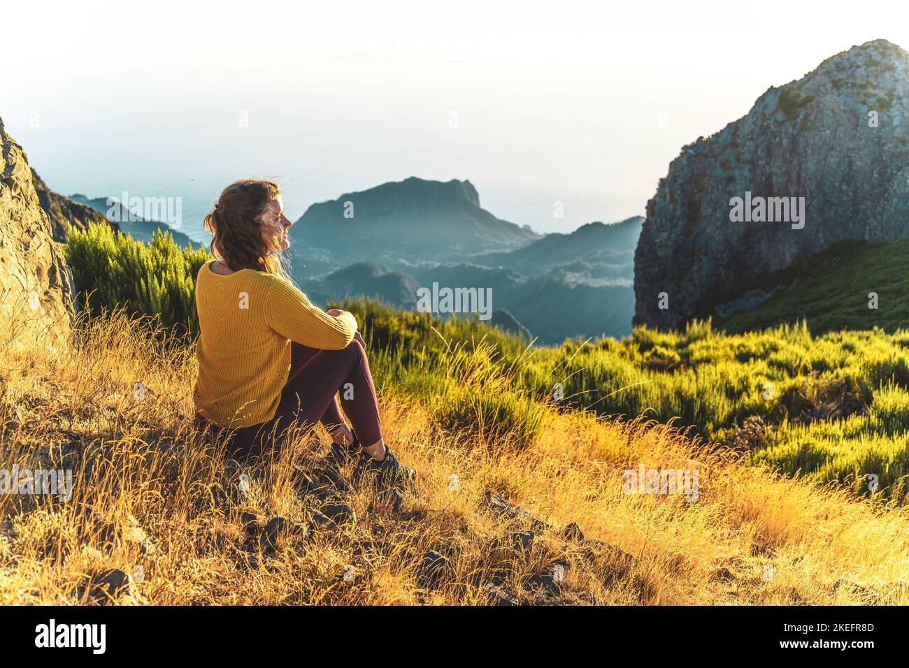 Descrizione: Donna seduta su un prato di montagna godendo il bellissimo paesaggio di montagna di Pico do Ariero all'alba. Pico do Arieiro, isola di Madeira Foto Stock