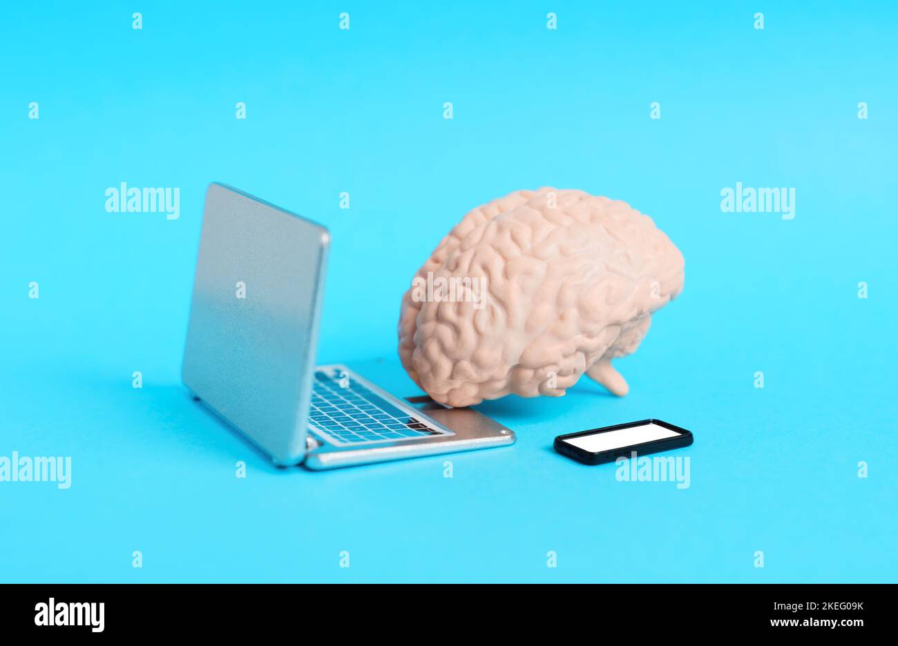 Cervello umano giocattolo posto da mini computer portatile e smartphone figurine isolato su sfondo blu. Foto Stock