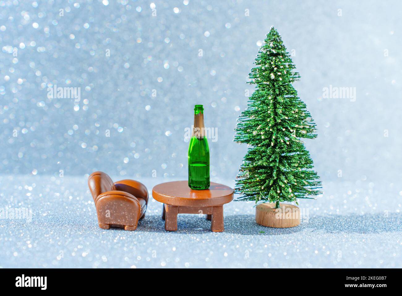 Mini biglietto del mattino del nuovo anno mondiale: Piccola bottiglia di champagne posta su un tavolo da salotto da un albero di Natale giocattolo su uno sfondo scintillante. Foto Stock