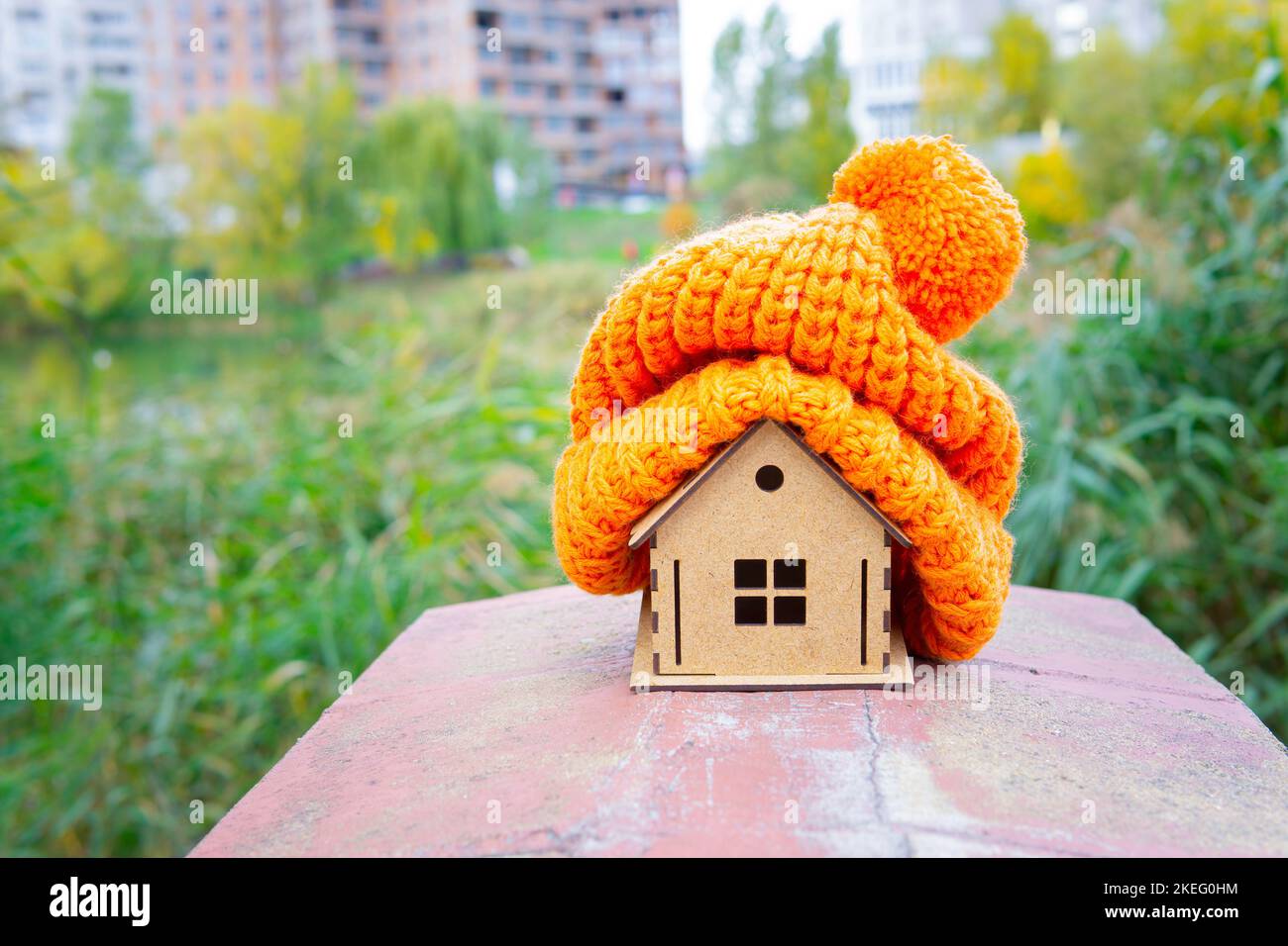 Piccolo modello di casa in legno con un cappello pompon arancione lavorato a maglia sulla parte superiore. Mantenere la casa calda mentre ritarda mettere il riscaldamento su. Foto Stock