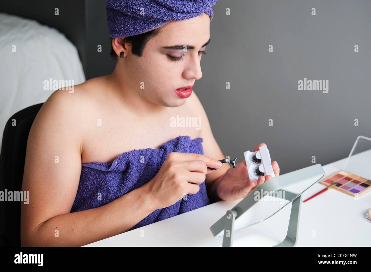 Giovane uomo transgender che applica ciglia false. Foto Stock