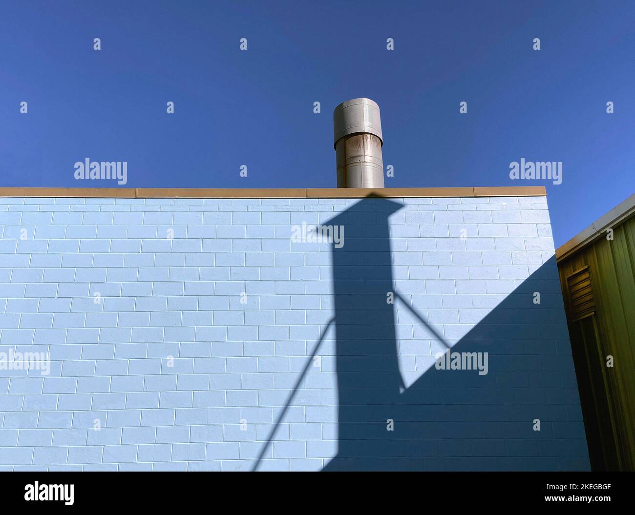 Uscita di scarico in metallo sul tetto dell'edificio Blue Cinder Block, Shadows on Wall Foto Stock