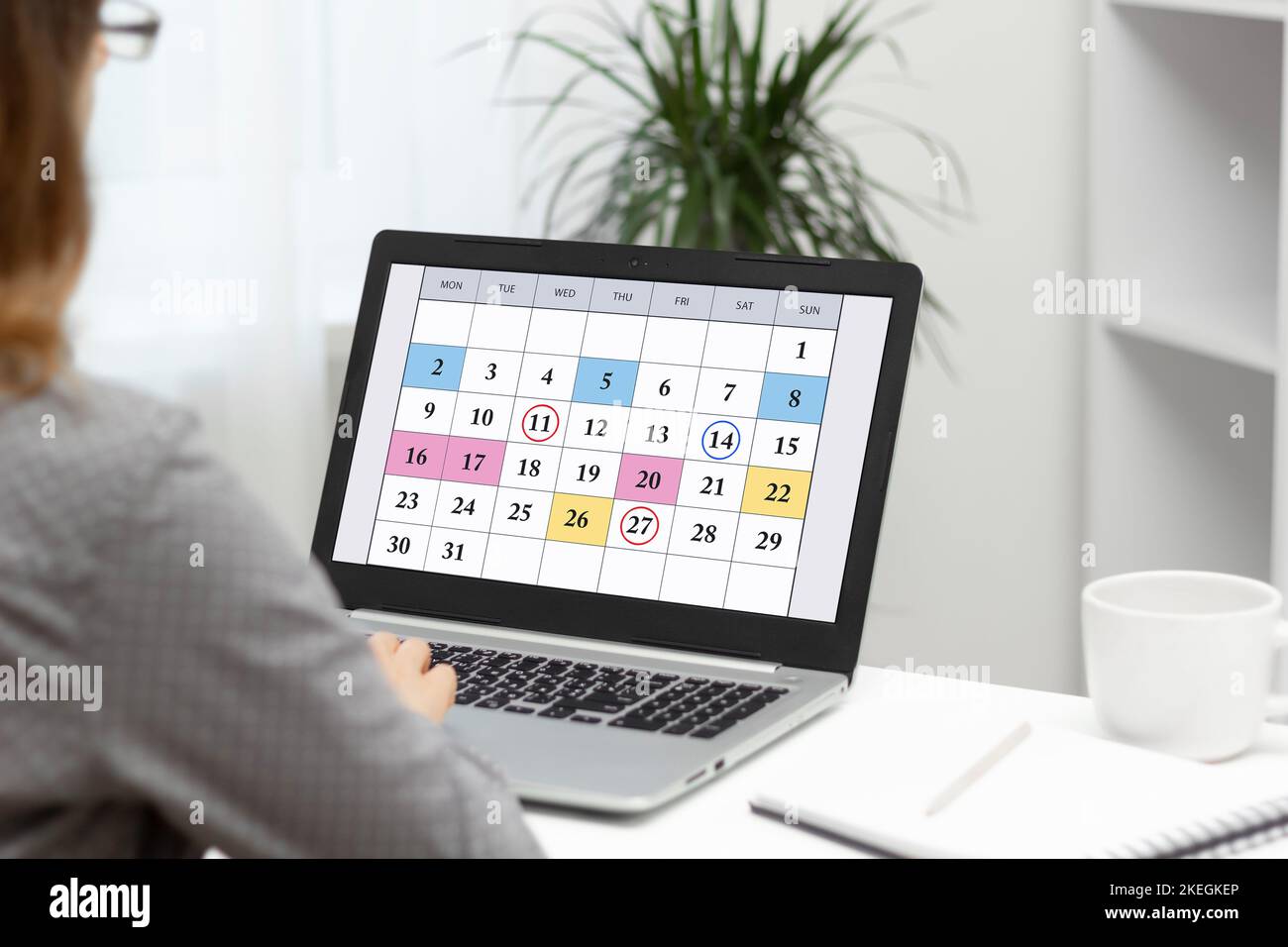 Donna che pianifica riunioni aziendali mensili, pianificazione e obiettivi utilizzando il calendario sul notebook. Foto Stock