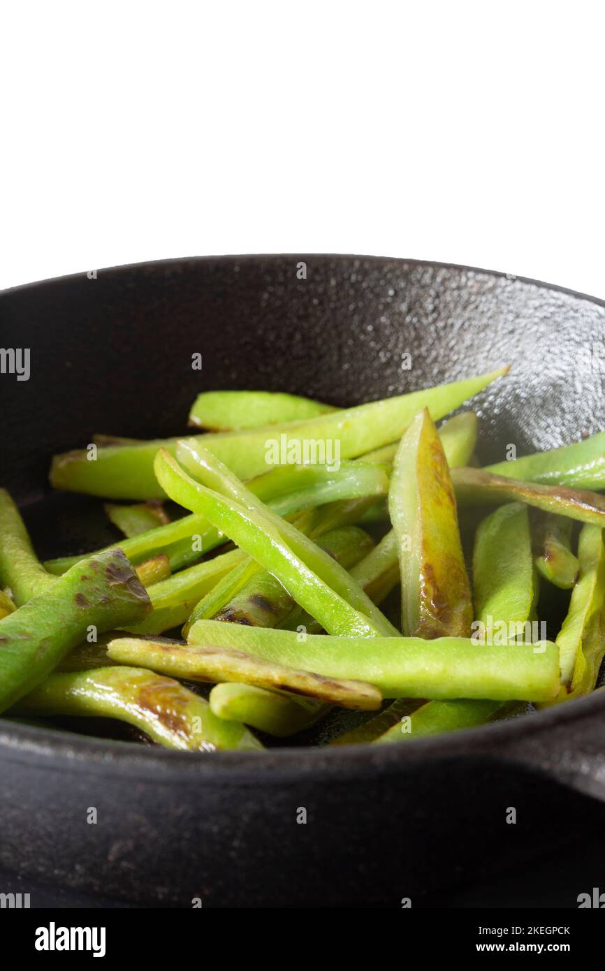 Fagiolini fritti, in una padella di ghisa, con olio d'oliva, su una tavola di ardesia. Isolato su sfondo bianco Foto Stock