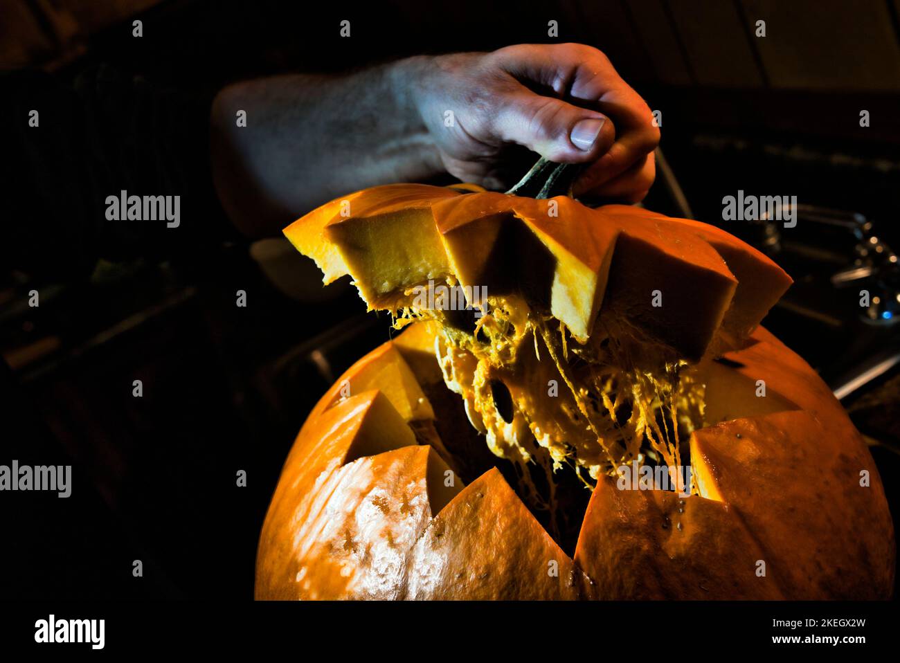 La parte superiore è sollevata da una zucca di Halloween che è scolpita in una cucina scura. Foto Stock