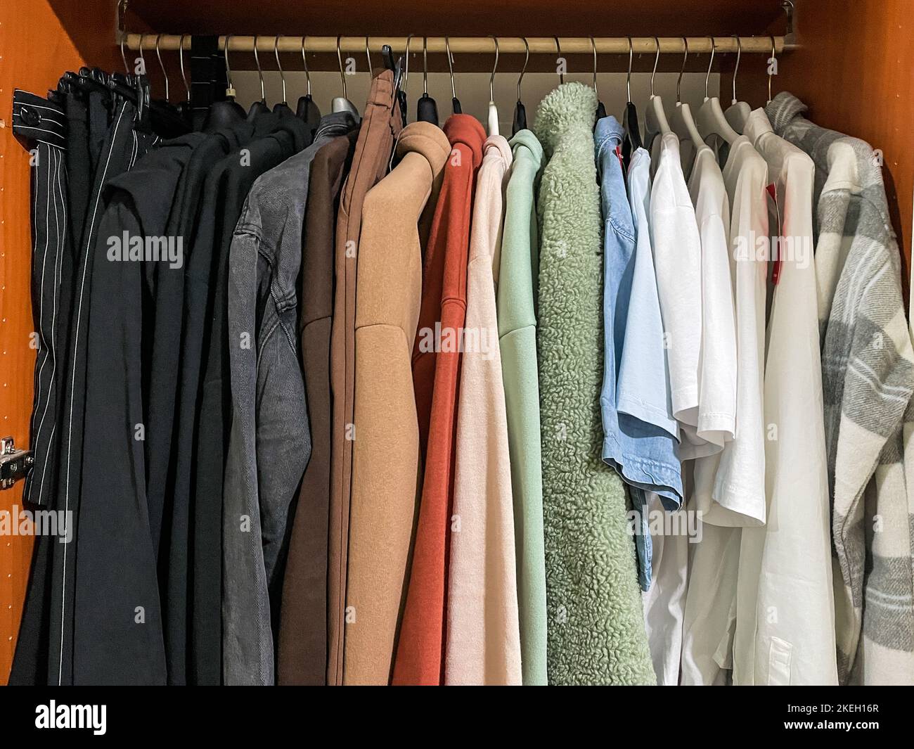 Varietà di abiti casual ragazza adolescente di diversi colori su grucce in guardaroba di legno Foto Stock