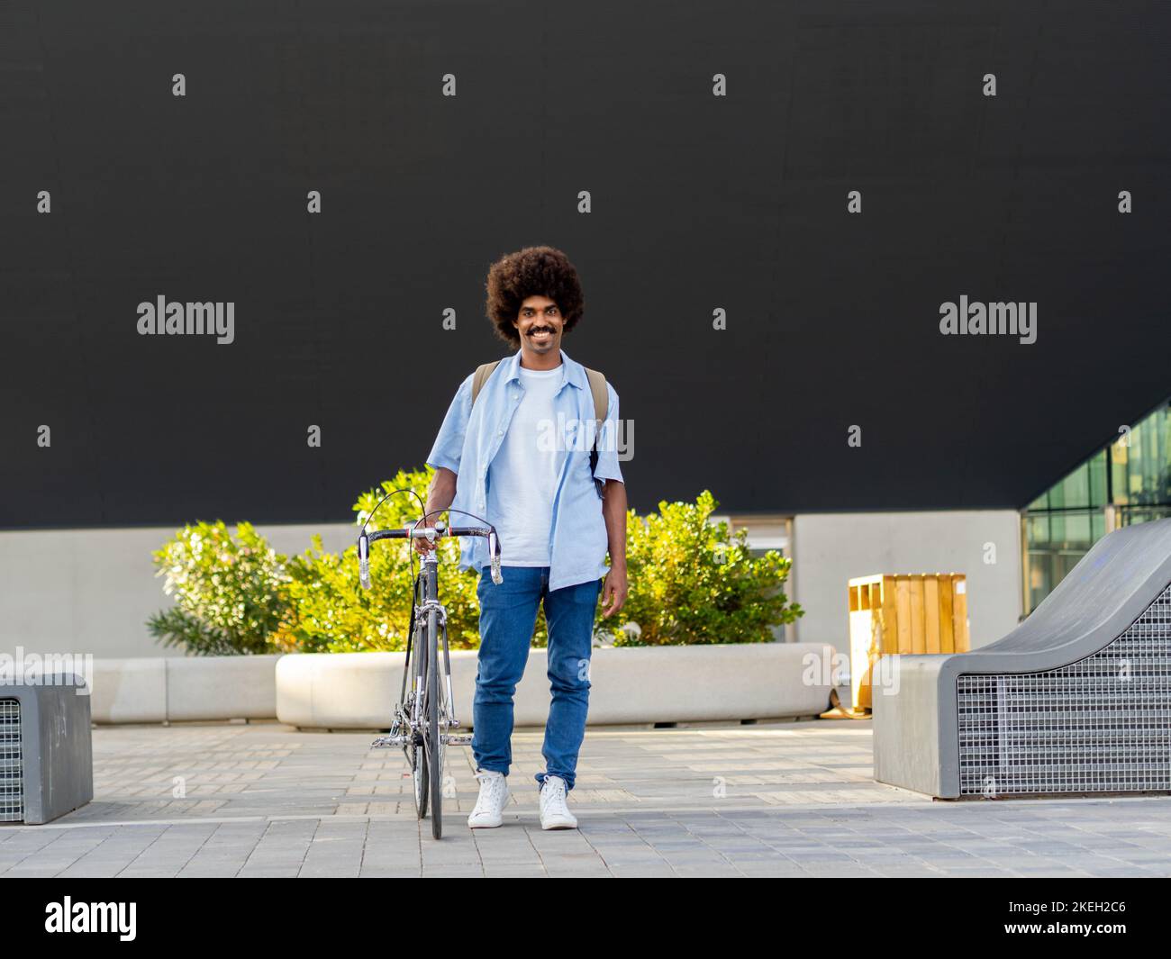 Giovane afro-americano sorridente con capelli afro in un quartiere finanziario con una bicicletta guardando la macchina fotografica Foto Stock