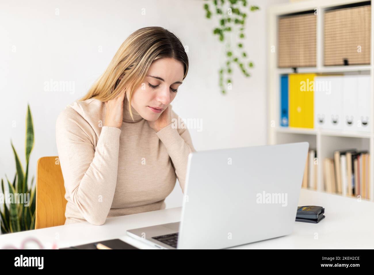 Una giovane donna in viaggio d'affari che soffre di dolore al collo quando lavora sul notebook a casa Foto Stock