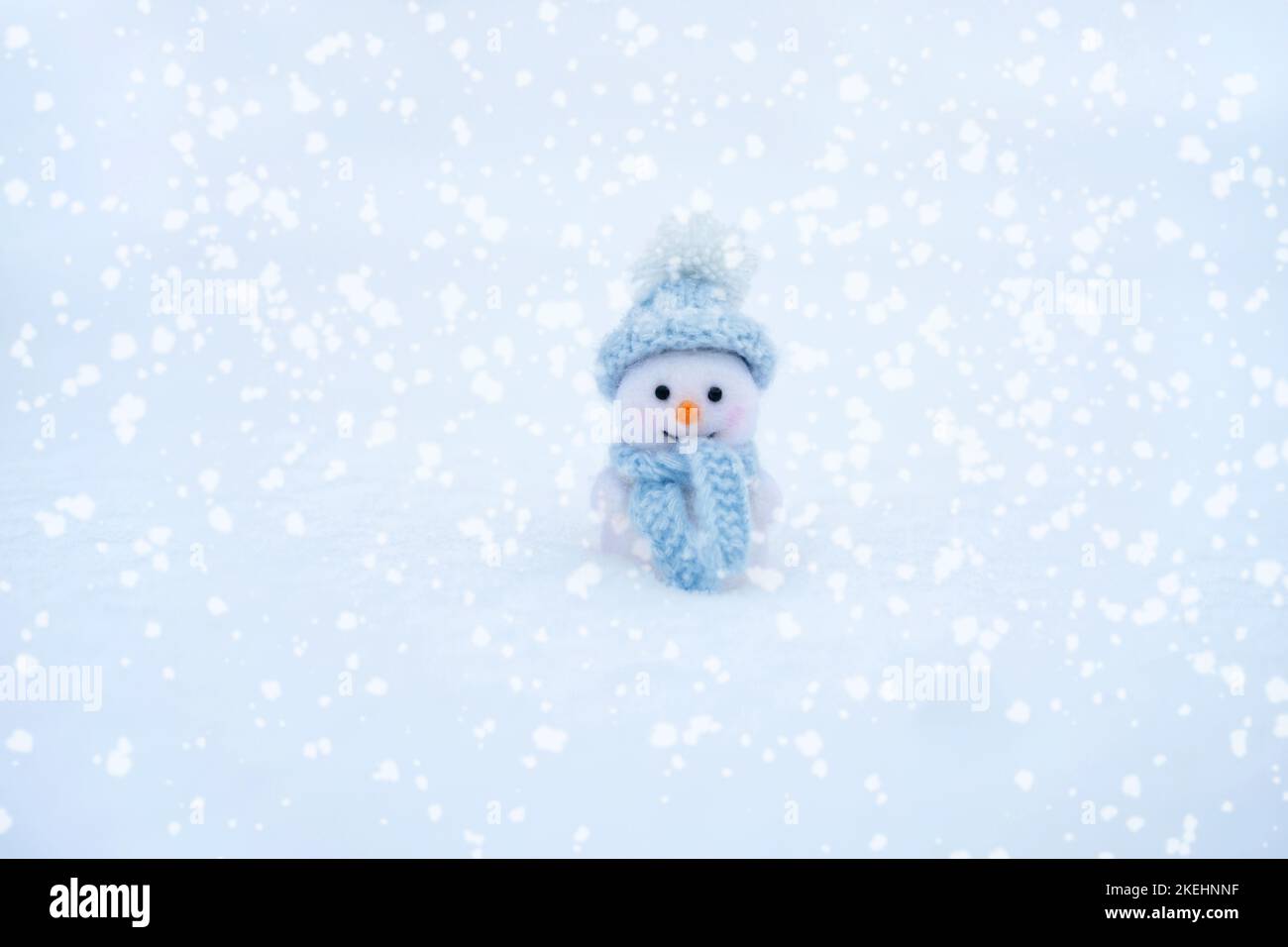 Simpatico pupazzo di neve giocattolo in un cappello blu e sciarpa su uno sfondo innevato. Auguri di Natale e Capodanno. Concetto invernale. Spazio di copia. Foto Stock