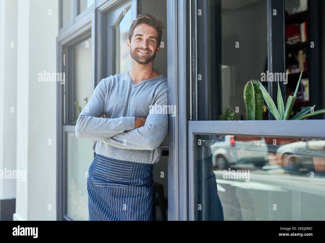 Il vostro cordiale (e simpatico) barista locale, un giovane bello e sicuro che sta alla porta della sua attività. Foto Stock