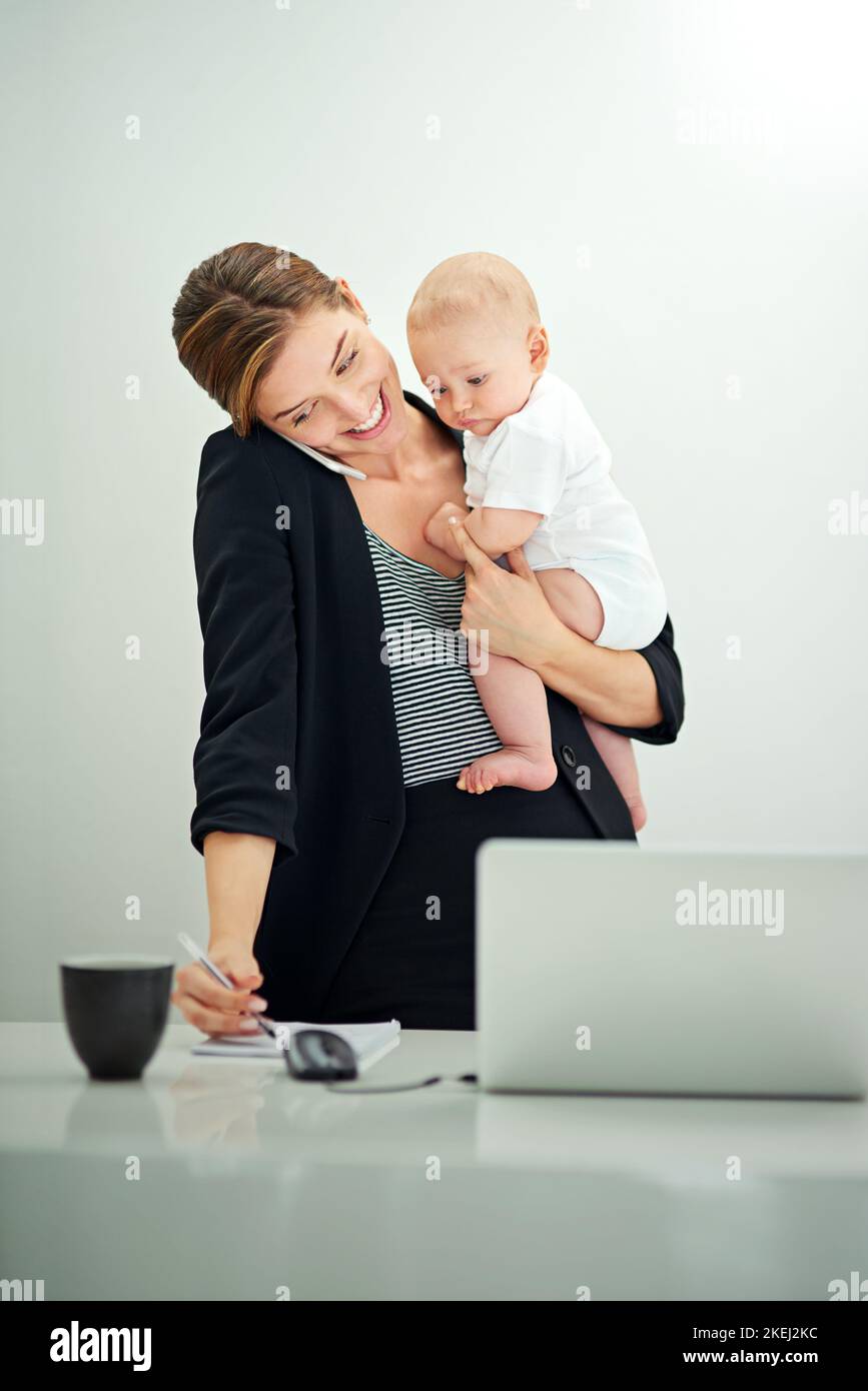 Costruire un impero d'affari per la sua famiglia. Una giovane donna d'affari di successo che trasporta il suo adorabile bambino ragazzo mentre parla al telefono. Foto Stock