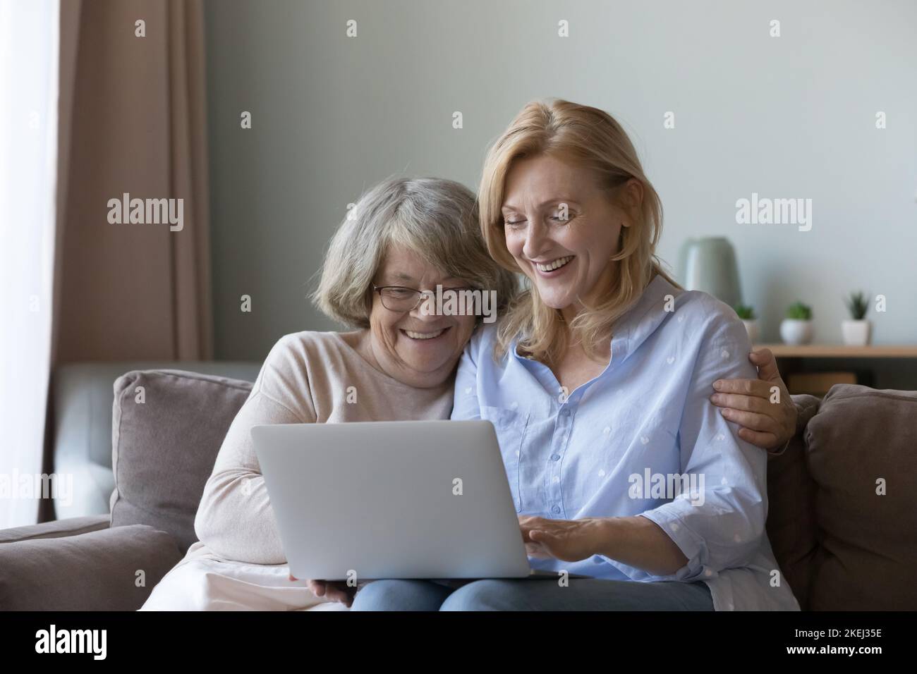 La figlia matura e la madre anziana siedono sul divano con il laptop Foto Stock