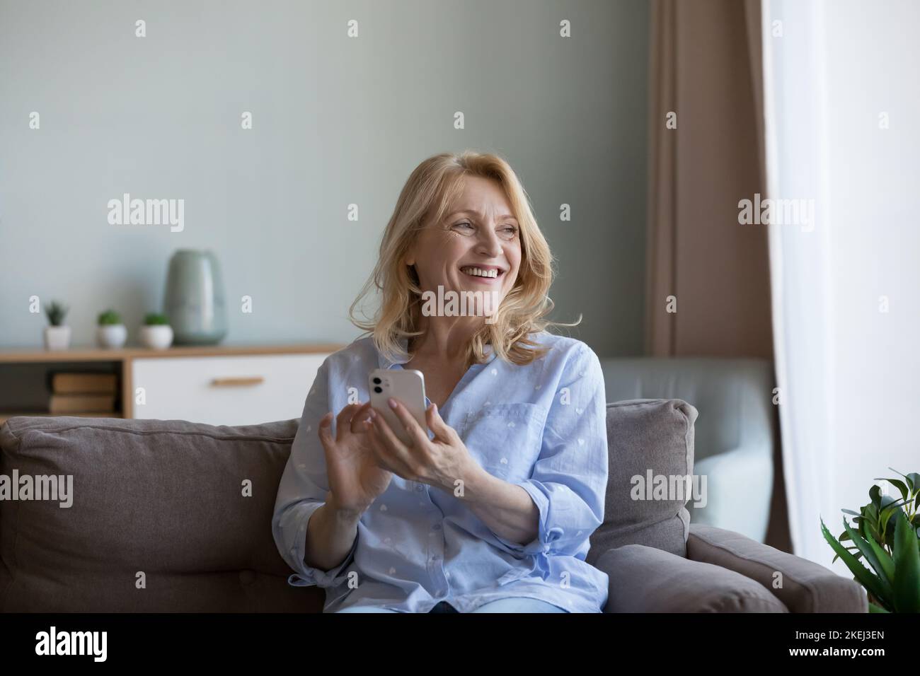 Felice donna matura seduta sul divano con smartphone Foto Stock