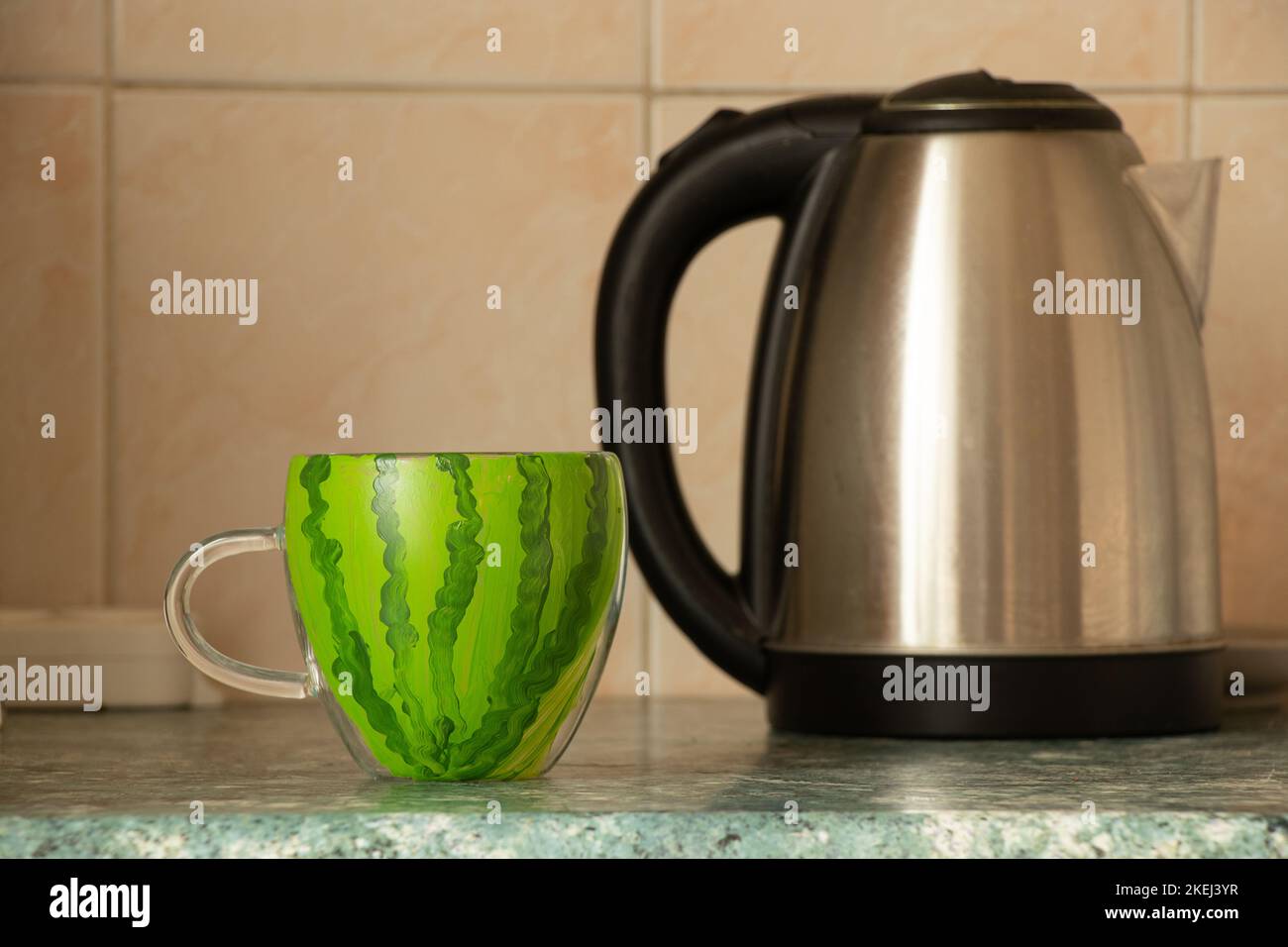 Una tazza con l'immagine di un anguria si trova su un tavolo in cucina vicino a un bollitore in Ucraina in un appartamento, la liberazione di Kherson, la guerra in Foto Stock