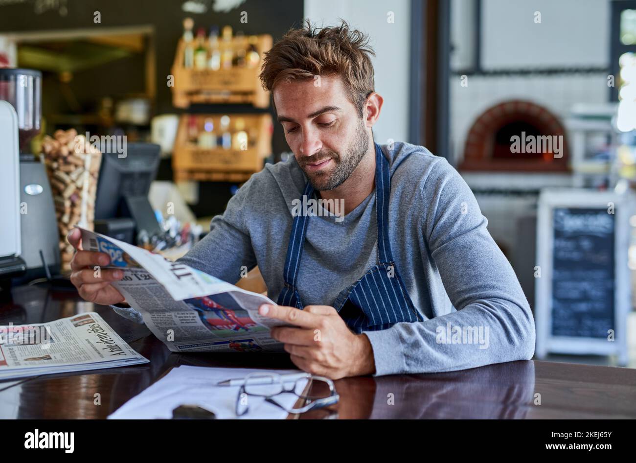 Un bel giovane seduto in un bar che legge un giornale. Foto Stock