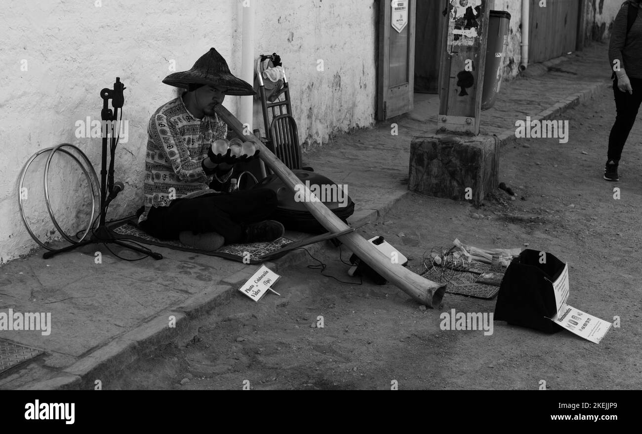 Una scala di grigi di un uomo che fuma il suo tubo di bambù mentre si siede a terra in Atacama Foto Stock