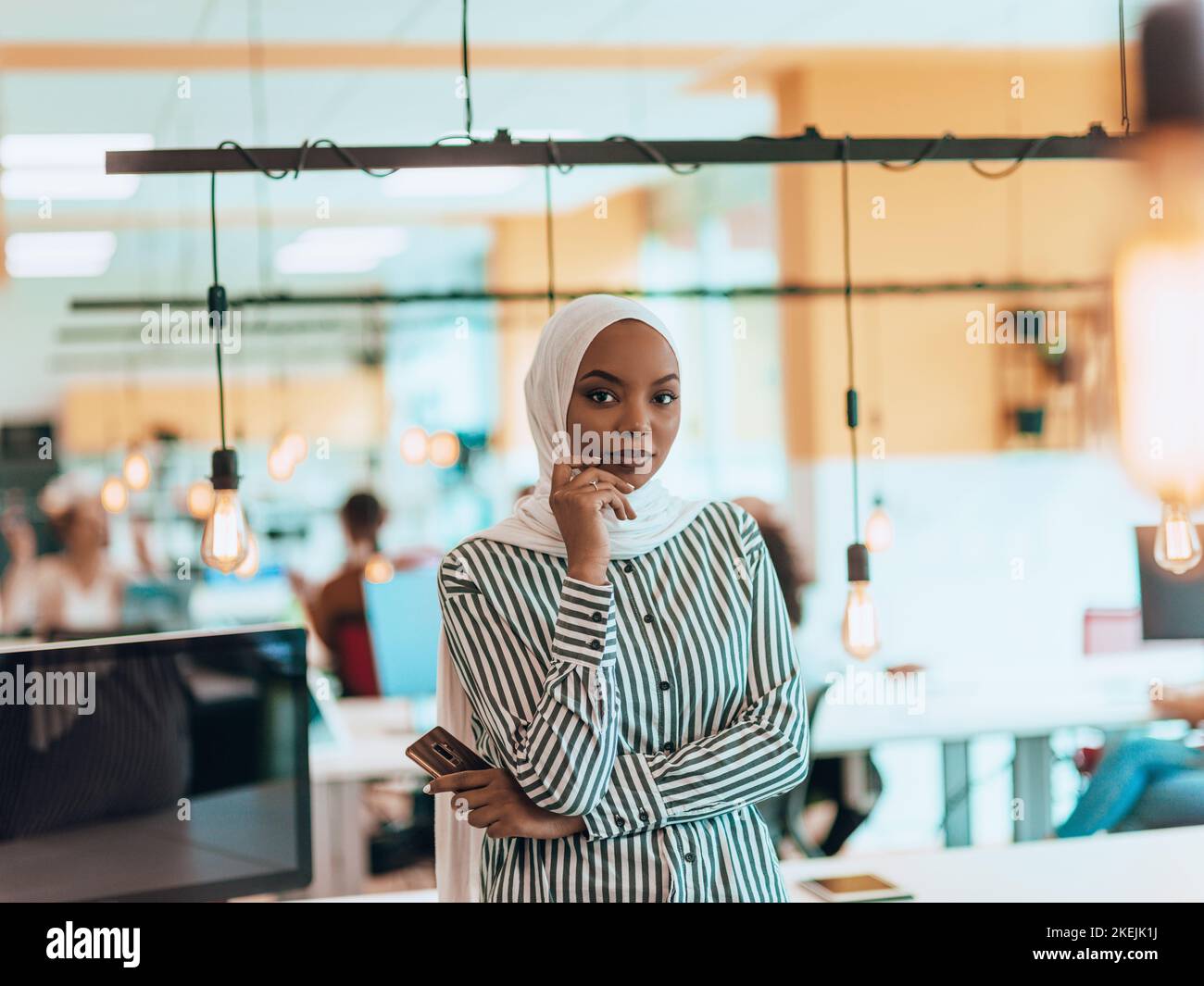 Protarit di una donna musulmana nera (afro-americana) in piedi in un moderno ufficio d'affari mentre indossa un hijab. Foto Stock