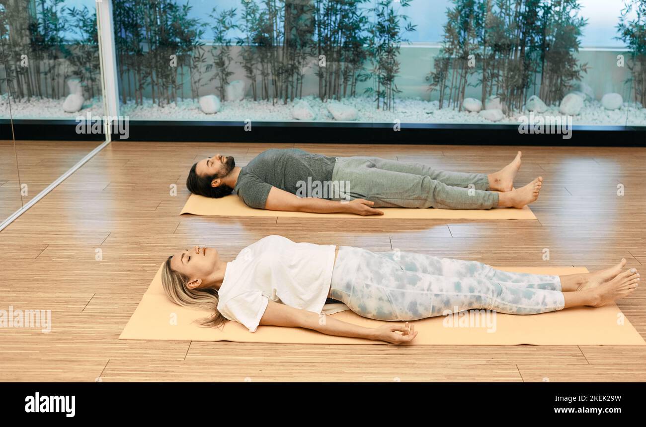 Fitness coppia in abbigliamento sportivo pratica yoga mentre sdraiati in savasana o in posa cadavere presso il centro yoga. Shavasana è posa importante nello yoga rigenerativo Foto Stock