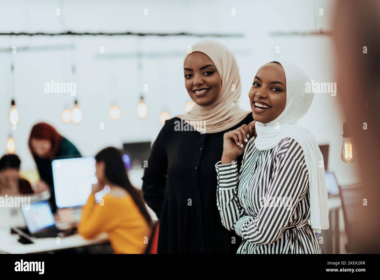 Ritratto di due donne d'affari afroamericane che parlano tra loro mentre si trovano in un moderno ufficio commerciale con i loro colleghi. Marketing Foto Stock