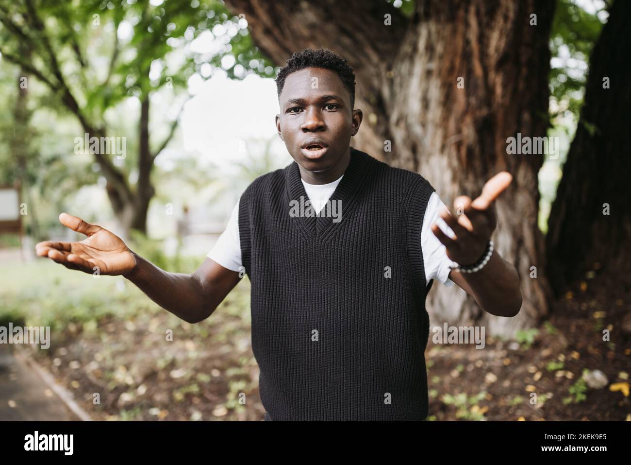 Scioccato sorpreso giovane africano con le mani in su in parco o strada. Giovane maschio frustrato che grugge le spalle, non capisca che cosa happend. Stagione autunnale o primaverile. Espressione del volto con le mani in alto Foto Stock