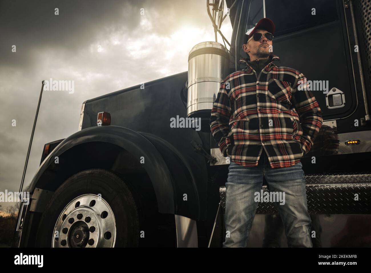 Caucasico Commercial semi Truck driver nel suo 40s davanti a un veicolo. Tema trasporto a terra. Foto Stock