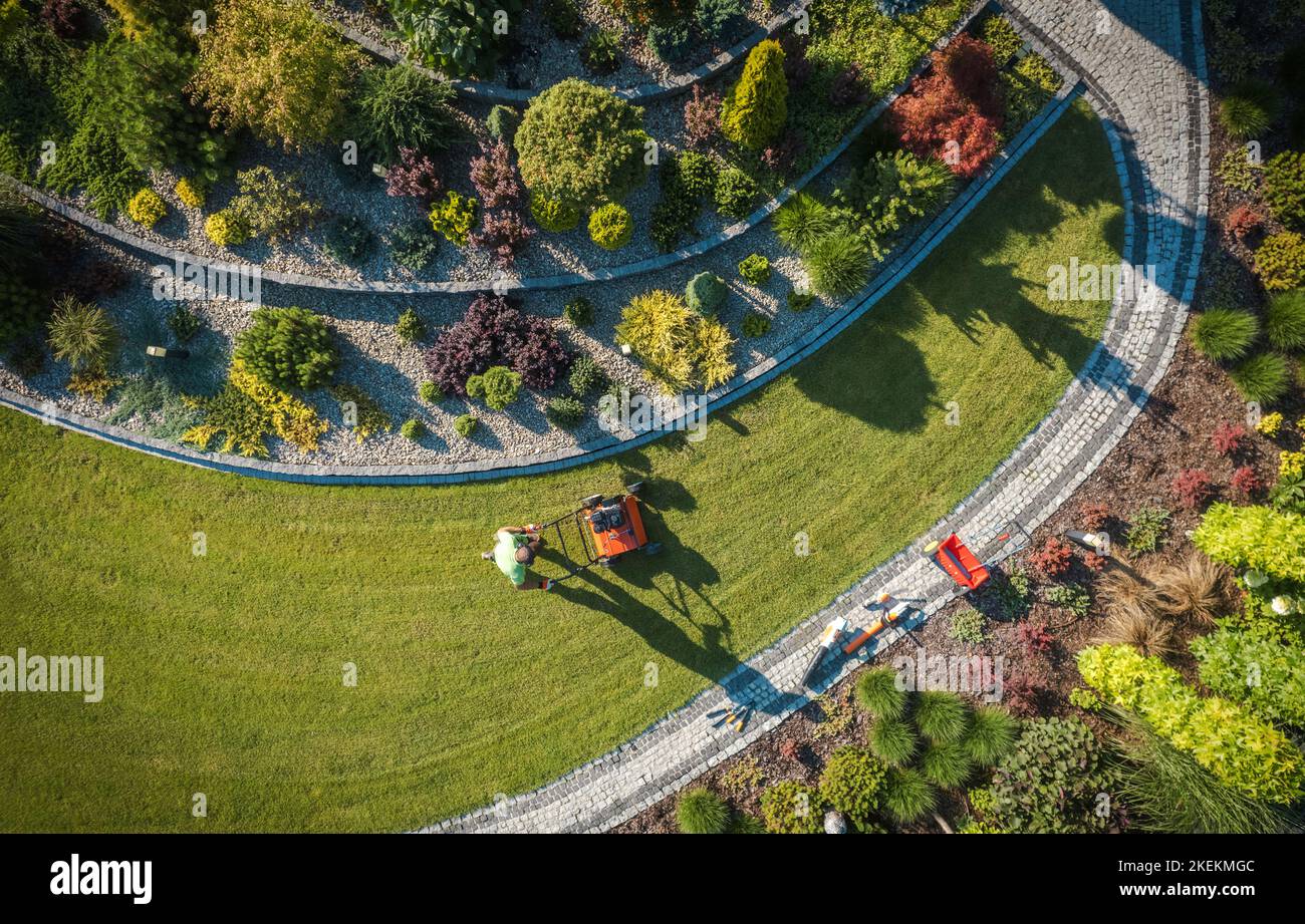 Vista aerea di un professionista che si adora al giardino con push Spreader. Tema fertilizzante prato. Giardinaggio e paesaggistica industria. Foto Stock