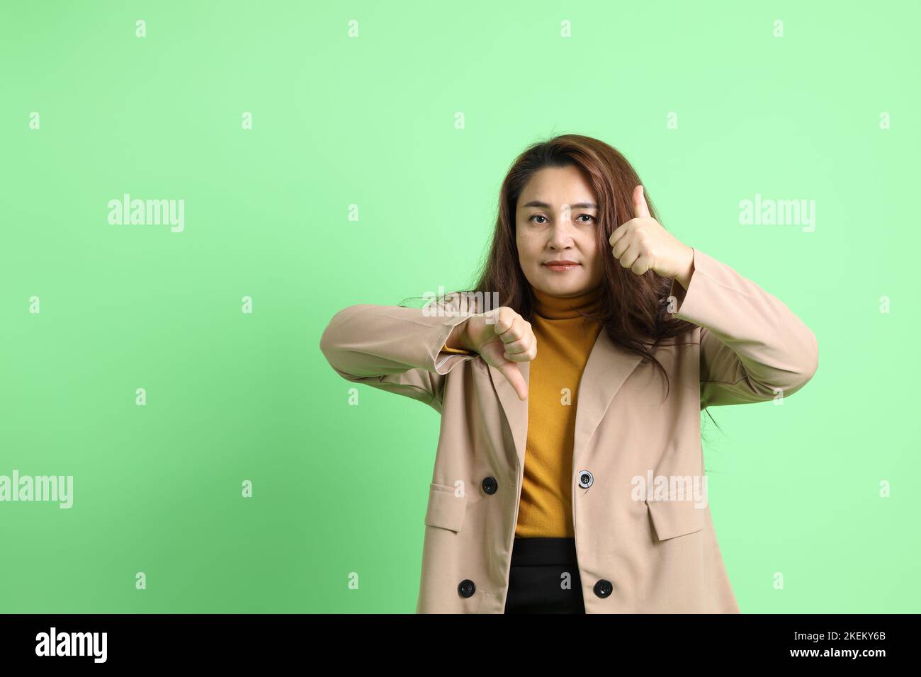 La donna asiatica d'affari adulta in piedi sullo sfondo verde. Foto Stock