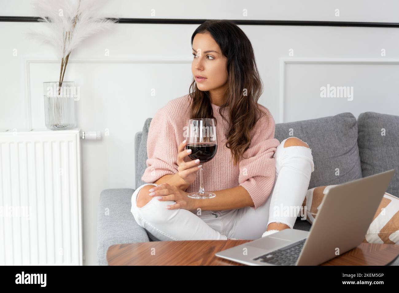 Donna seduta sul divano, riposante con un bicchiere di vino rosso Foto Stock