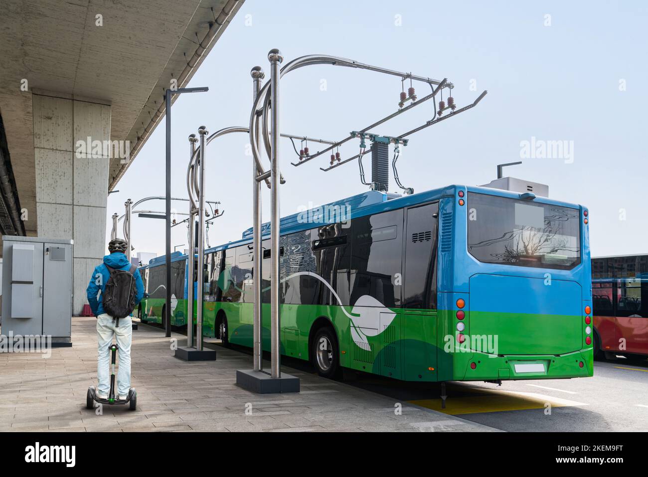 L'uomo a bordo di uno scooter elettrico accanto all'autobus elettrico in una fermata viene addebitato dal pantografo. Foto Stock
